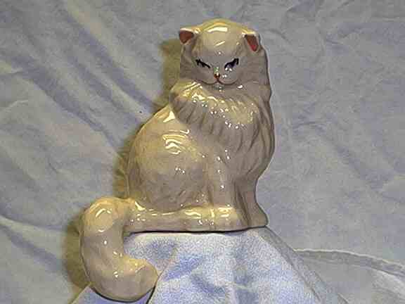 Photo of figurine of white cat with tail hanging over edge