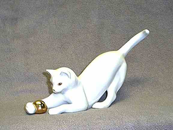 Photo of figurine of white cat playing with gold ball